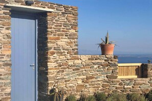A stone building with a blue door, a potted plant, and a view of the sea. - Felicia Exclusive Villa - Private Pool (Tinos)