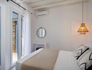 A bedroom with a bed, a round mirror, a hanging lamp, and a stone wall. - Felicia Exclusive Villa - Private Pool (Tinos)