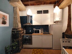 Cocina compacta con microondas, horno y lavamanos, paredes de piedra y lámparas colgantes.