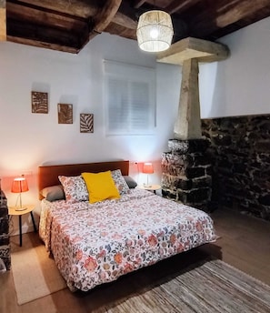 Un dormitorio con cama, dos lámparas de noche, una pared de piedra y una lámpara colgante.