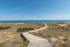 Ein hölzerner Steg führt zu einem Strand bei blauem Himmel.