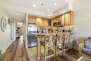 Una cocina con armarios de madera, un refrigerador de acero inoxidable, un microondas y una zona de bar con sillas de mimbre.