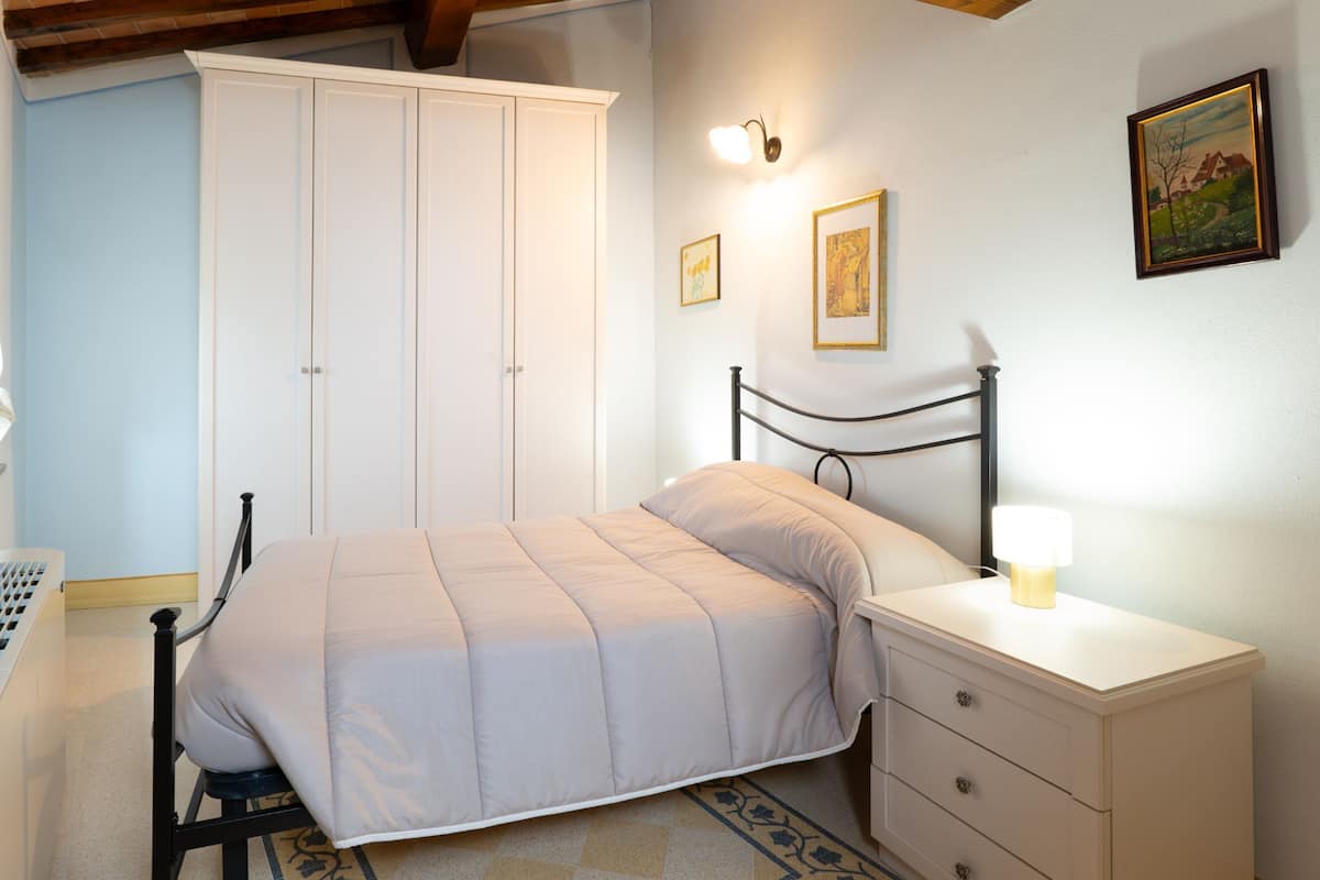 A bedroom with a bed, nightstand, dresser, wardrobe, and wall-mounted light fixtures.