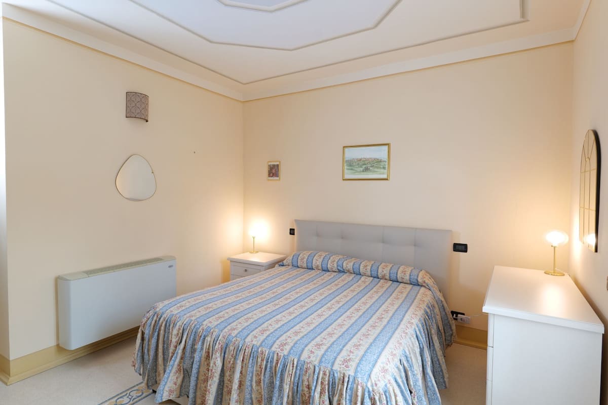 A bedroom with a bed, bedside tables, a radiator, and a wall-mounted picture.
