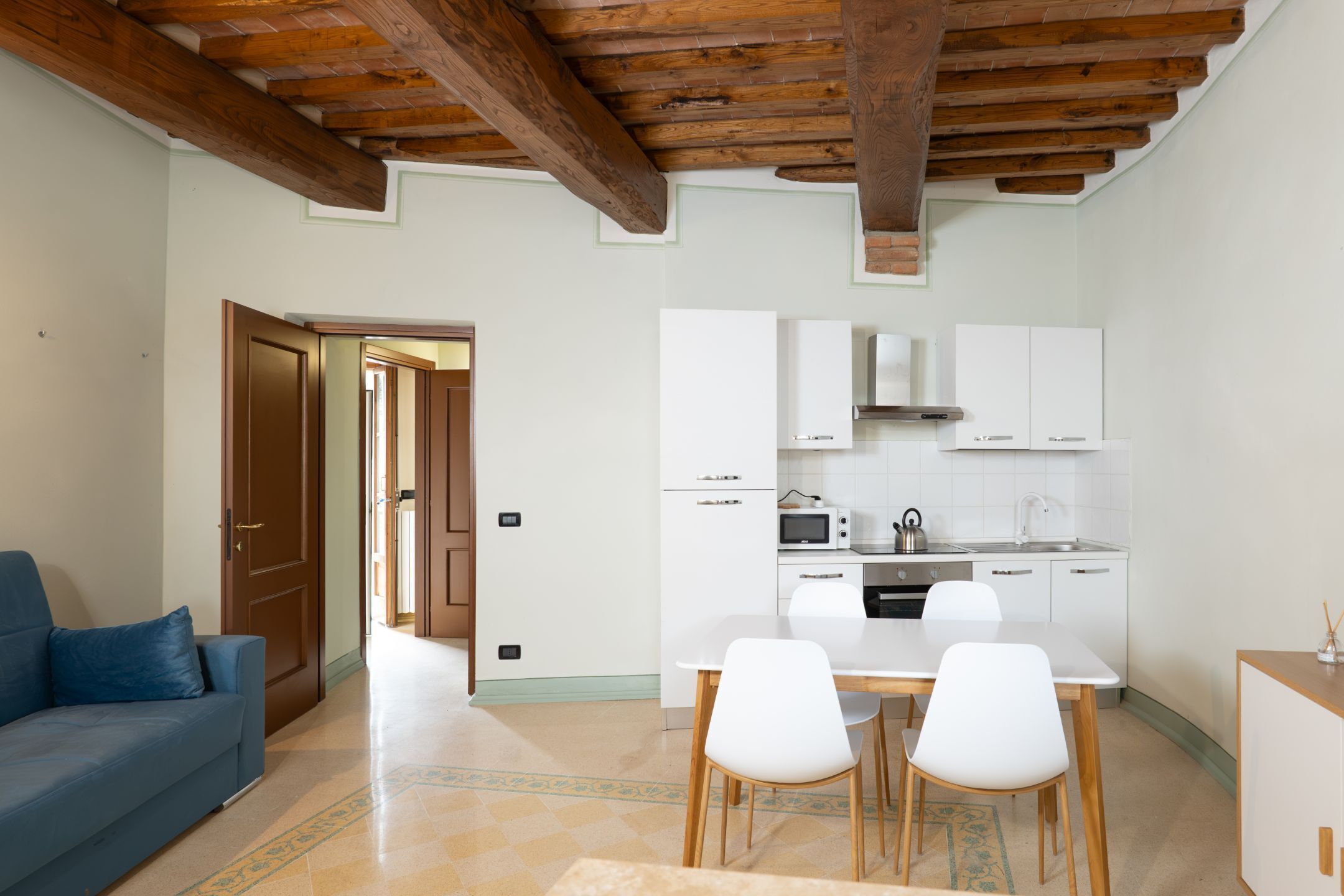 A compact living space with a kitchenette, a dining area with two chairs, a sofa, and a wooden ceiling.