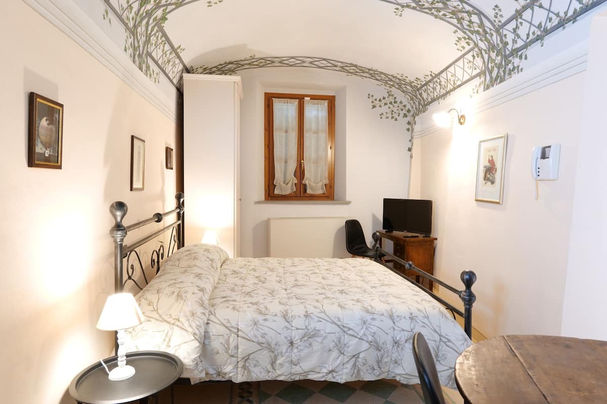A bedroom with a bed, a desk, a chair, a TV, and a window with curtains.