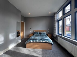 Quarto com cama, mesas de cabeceira, espelho e uma janela grande.