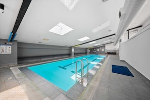 A swimming pool with a blue floor, metal handrails, and a tiled floor around it. - Spacious 3-bed Apartment in Canberra CBD (Canberra)