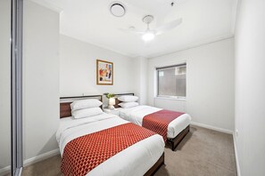 Habitación de hotel con dos camas, un ventilador de techo, una ventana y un cuadro en la pared.