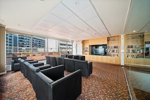 A spacious indoor area with black leather seating, a patterned carpet, and a large window offering a view of buildings outside. - Spacious 3-bed Apartment in Canberra CBD (Canberra)