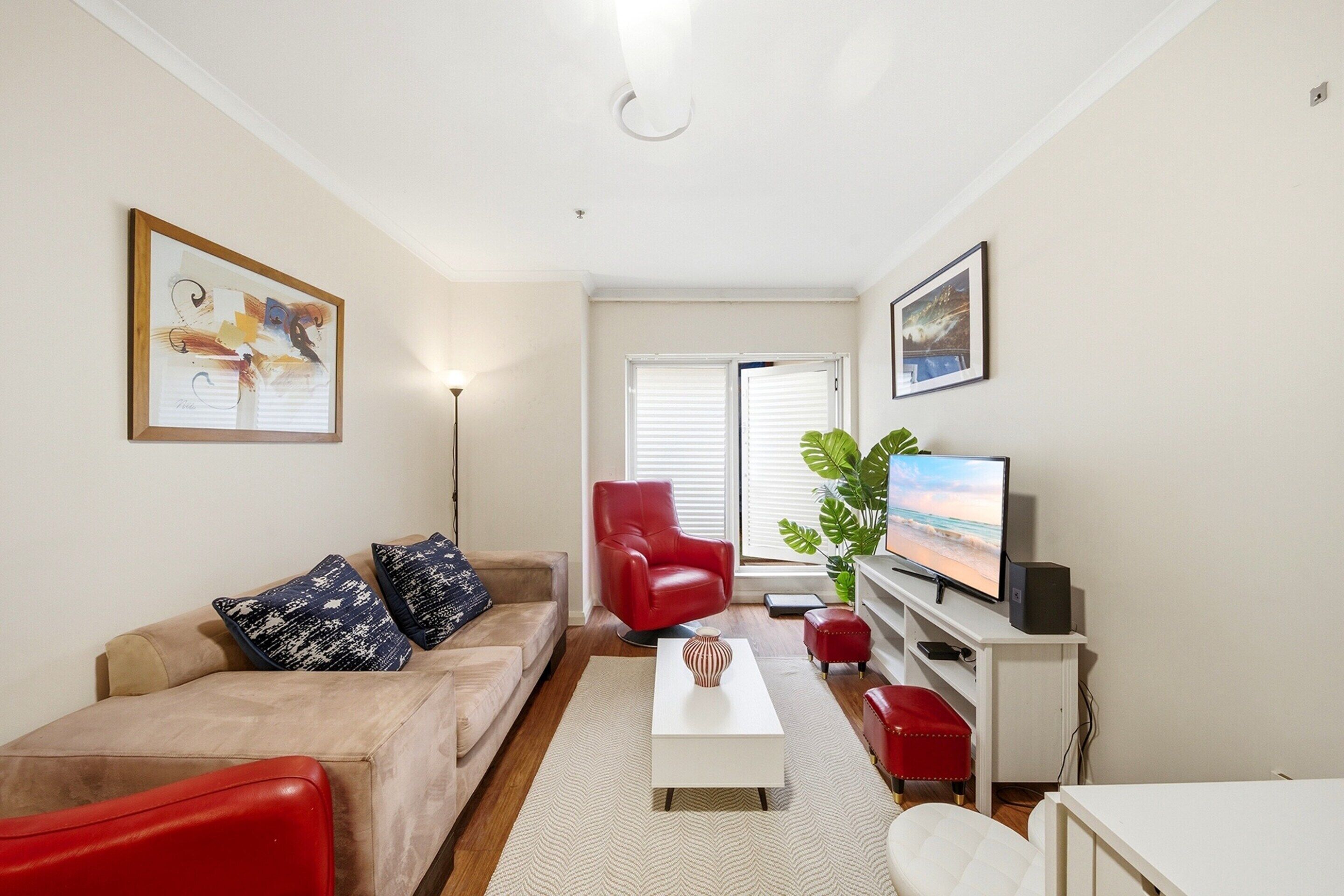 A living room with a sofa, red armchair, coffee table, TV, and a plant.