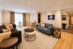Ein modernes Wohnzimmer mit einer Couch, zwei Couchtischen, einem Fernseher und einem Gemälde an der Wand.