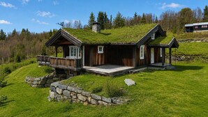 A wooden house with a grass roof, a stone wall, and a deck. - Cosy mountain cabin in Golsfjellet (Gol)