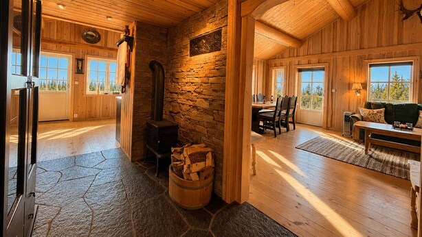 A log cabin interior with a stone fireplace, wooden floors, and large windows. - Cosy mountain cabin in Golsfjellet (Gol)