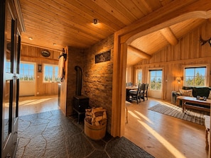 A log cabin interior with a stone fireplace, wooden floors, and large windows.