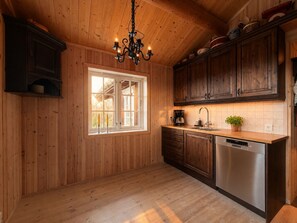 A kitchen with wooden walls, a window, a chandelier, and a dishwasher.