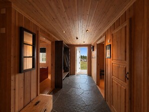 A wooden hallway with a bench, a door leading outside, and a stone floor.