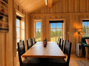 A wooden interior with a long dining table, chairs, and a heater.
