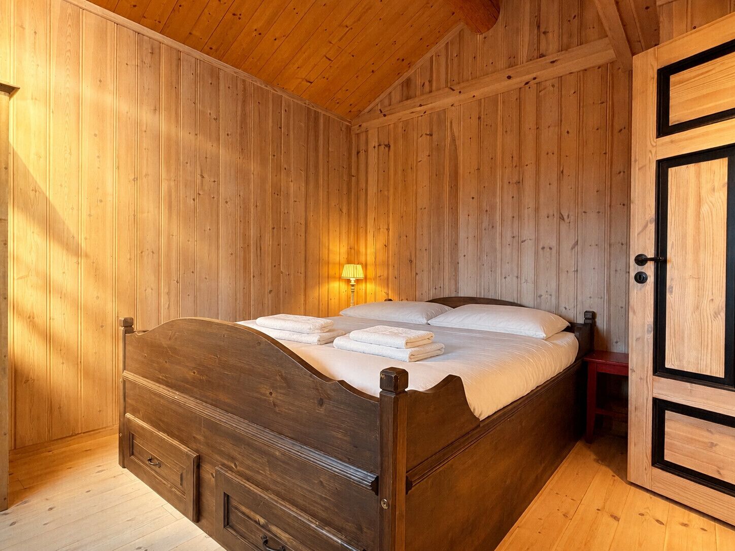 A wooden-paneled room with a bed, a nightstand, and a door.