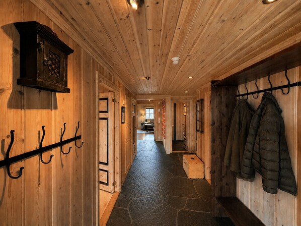 A wooden hallway with a stone floor, coat hooks, and a coat rack.
