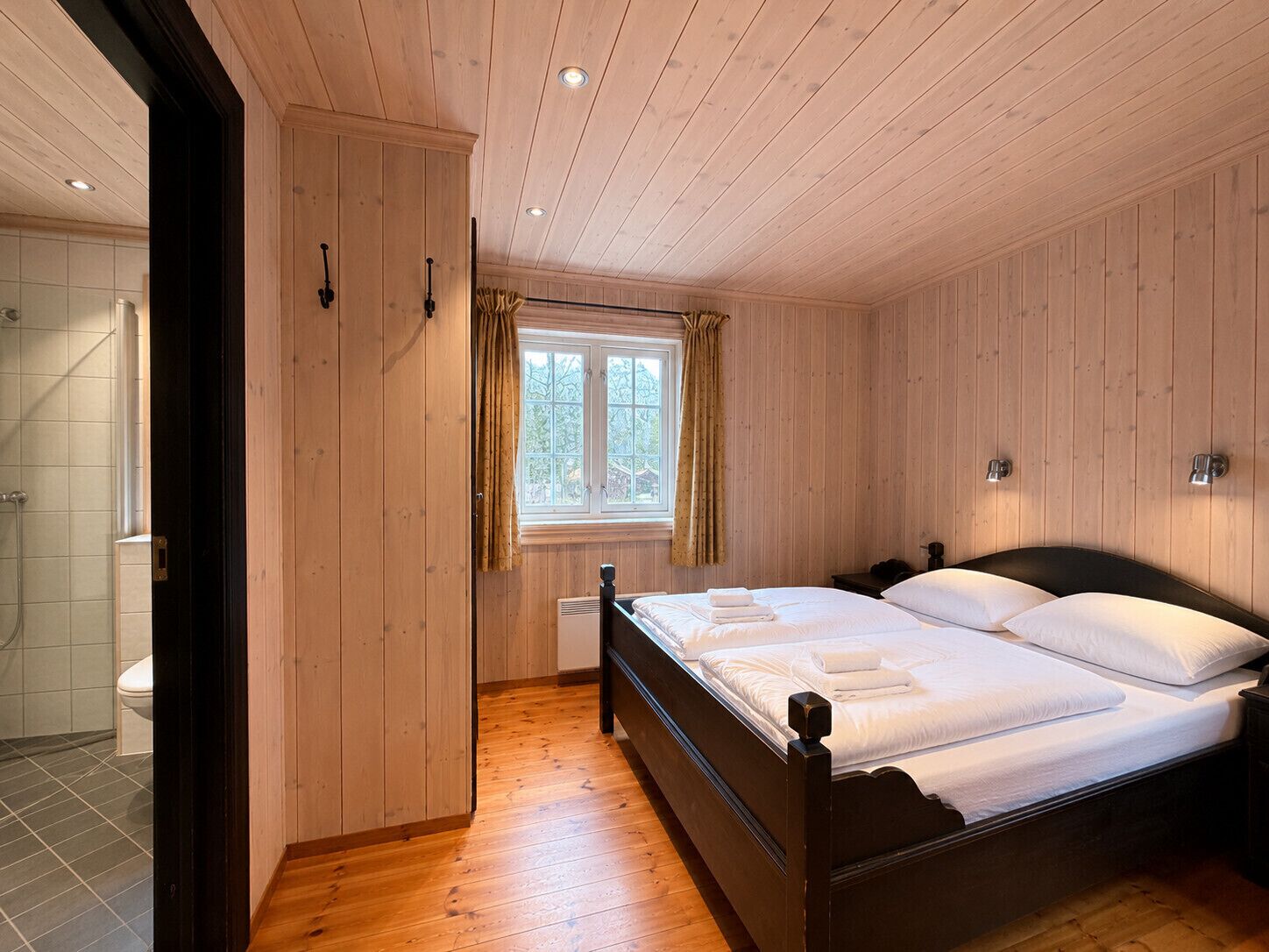 Un dormitorio con paneles de madera, una cama, un ventanal con cortinas y una zona de ducha.