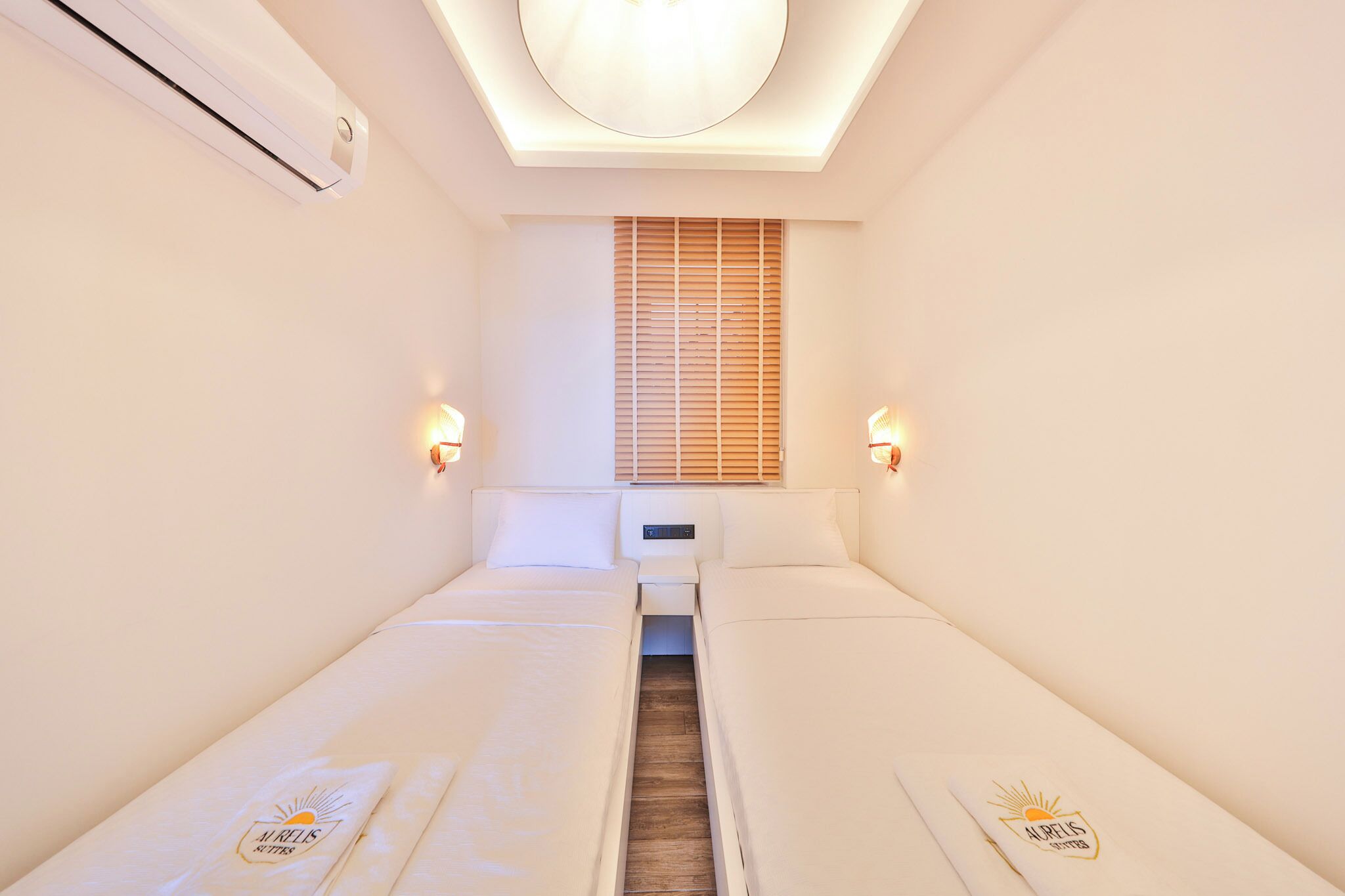 Ein Hotelzimmer mit zwei Betten, einer Deckenleuchte, einem Fenster mit Jalousien und Wandleuchten.