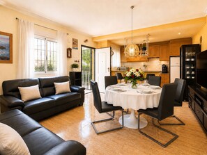 Ein Wohnzimmer mit einer Couch, einem Esstisch, Stühlen und einer Küche im Hintergrund.