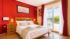 Una habitación de hotel con una cama, dos mesitas de noche, un ventanal con cortinas y una pared roja.