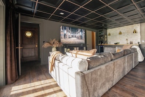 Un salon avec un grand canapé, un téléviseur et un mur en pierre agrémenté de luminaires suspendus.