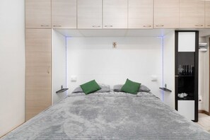 Une chambre à coucher comprenant un lit, deux oreillers, une table de chevet, une armoire et une étagÚre avec divers objets.