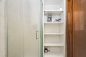 Une salle de bain avec une douche à parois de verre, un lavabo blanc et une étagÚre contenant des articles de toilette.