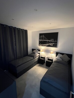 Une chambre dâhĂŽtel moderne, Ă©quipĂ©e dâun lit, dâun canapĂ©, de deux tables de chevet et dâun tableau reprĂ©sentant un pont, accrochĂ© au mur.