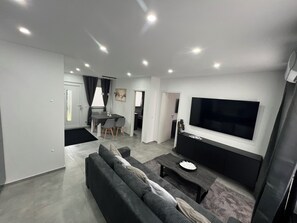 Un salon moderne comprenant un canapé, une table basse, un téléviseur et un coin repas avec des chaises et une table.