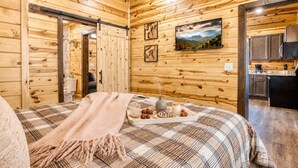 Een houten cabin met een bed, een eettafel met eten, een keukenhoek en een schilderij aan de muur.