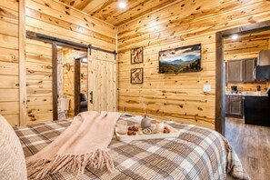 Ein Holzblockhaus-Interieur mit einem Bett, einem Esstisch gedeckt mit Speisen, einer Küchenzeile und einem Bild an der Wand.