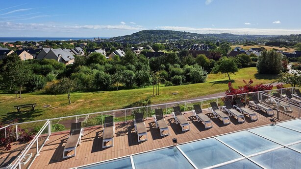 A rooftop deck with sun loungers, a pool, and a view of a residential area. - Sea View Houlgate Apartment for 4 (Houlgate)