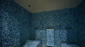 Habitación con paredes y suelo de mosaico azul, dos bancos y zona de ducha.