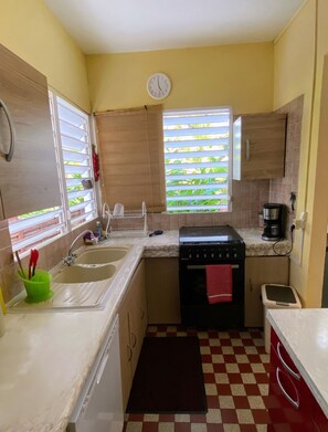 A compact kitchen with a sink, stove, and a clock on the wall. - House Simon Terrace Garden (Lamentin)