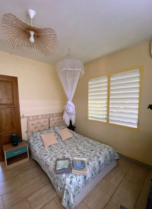 A bedroom with a bed, bedside table, nightstand, window with blinds, and a ceiling fan. - House Simon Terrace Garden (Lamentin)