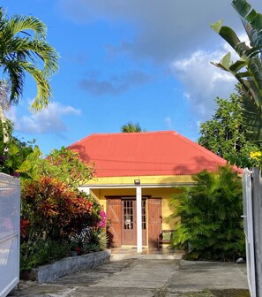 A house with a red roof, wooden doors, and a covered porch. - House Simon Terrace Garden (Lamentin)