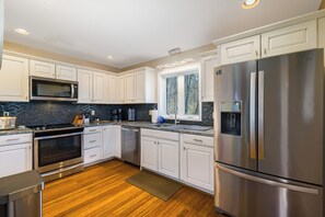 A modern kitchen with white cabinets, stainless steel appliances, a black backsplash, and a wooden floor.