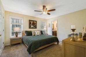 A bedroom with a bed, a ceiling fan, a window with blinds, a bedside table, and a nightstand.