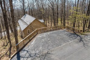 A cabin with a paved driveway and a wooden fence.