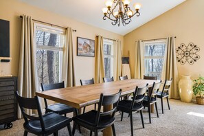 A dining room with a wooden table, black chairs, a chandelier, and large windows with curtains.