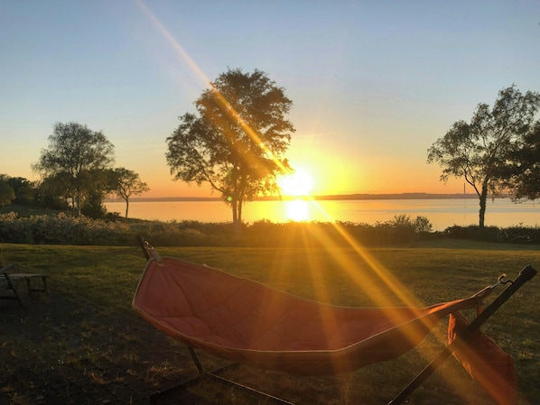 Un hamac dans une zone herbeuse, avec un coucher de soleil en arrière-plan.