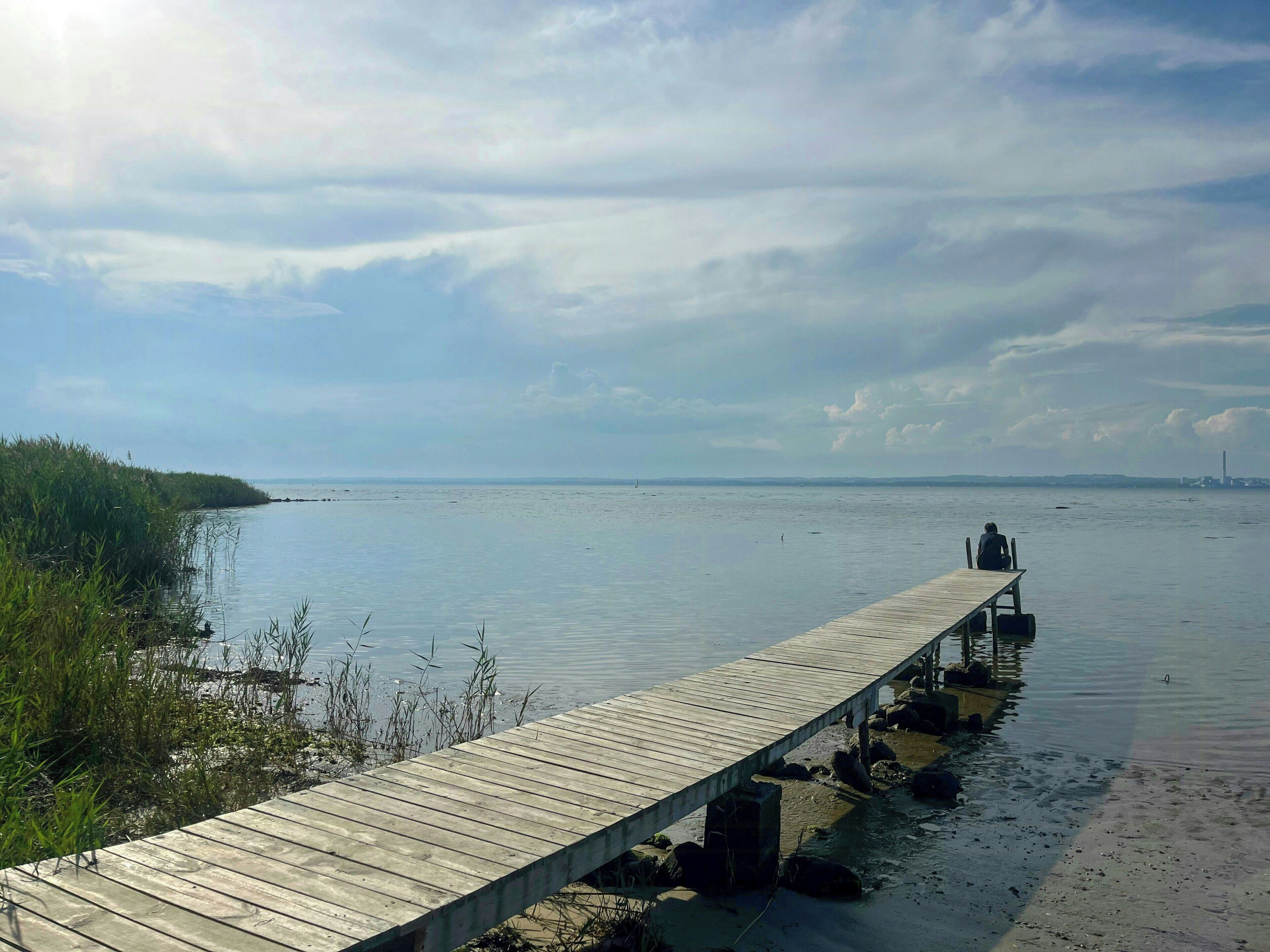 A wooden pier extending into calm water, with a person sitting at the end.