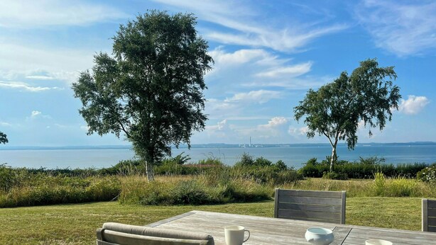 Ein Außenbereich mit Tisch und Stühlen, mit Blick auf ein Gewässer und das entfernte Land.