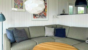 Ein modernes Wohnzimmer mit einer Eckcouch, einem runden Couchtisch aus Holz und einer Pendelleuchte.