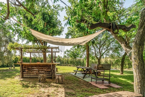 An outdoor seating area with a wooden table and benches, surrounded by trees and a hammock. - Podere Pala - Pet Friendly (Grosseto)
