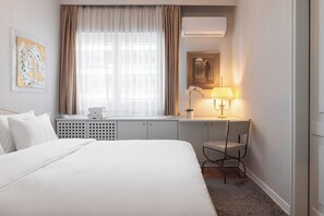 Ein Hotelzimmer mit einem Bett, einem Schreibtisch mit Lampe, einem Heizkörper und einem Fenster mit Vorhängen.
